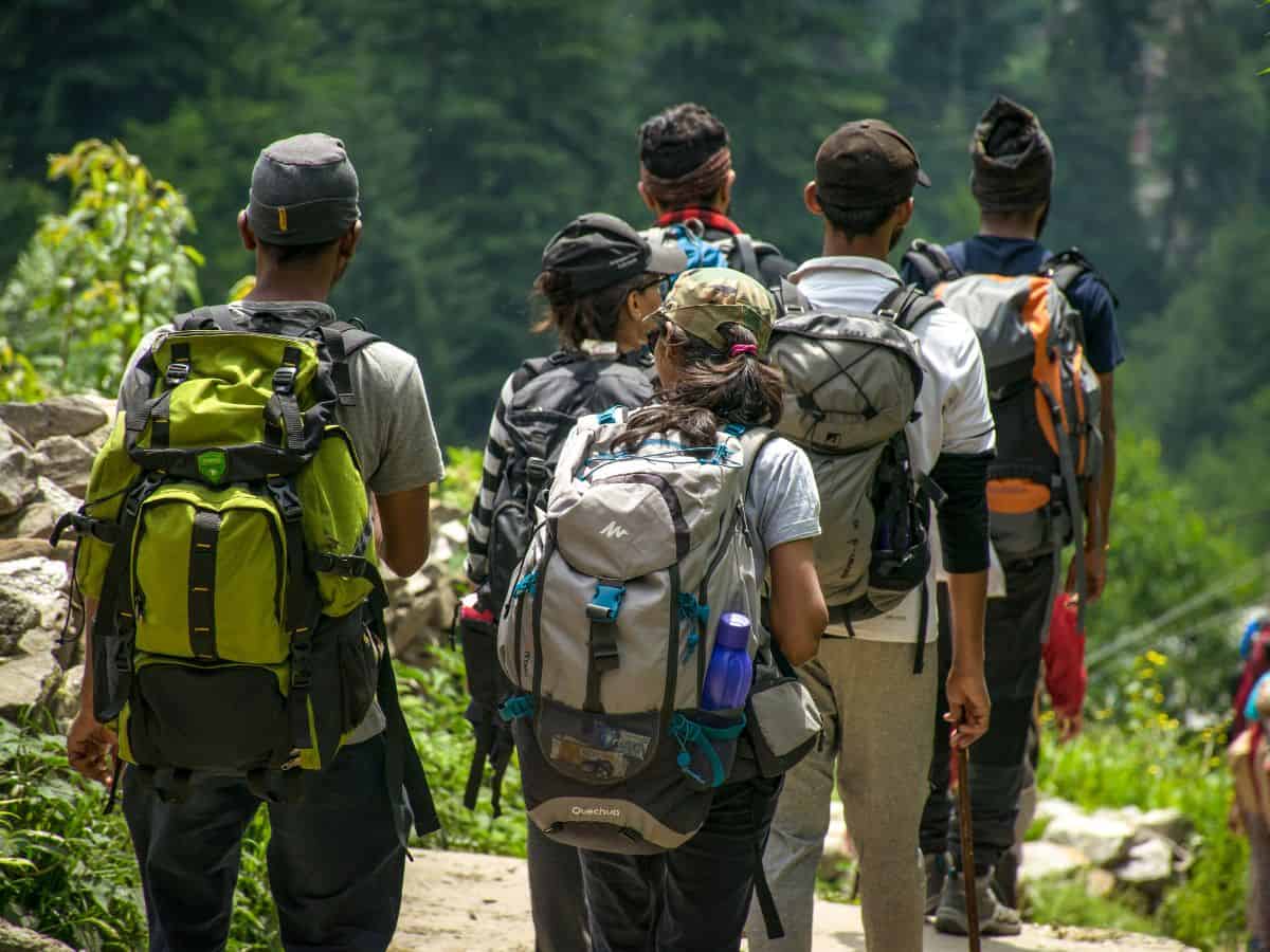 A group of hikers walking through a forested trail with backpacks, representing vacation and outdoor activities available in Denver vs San Francisco. The image highlights the natural beauty and recreational opportunities associated with these cities.
