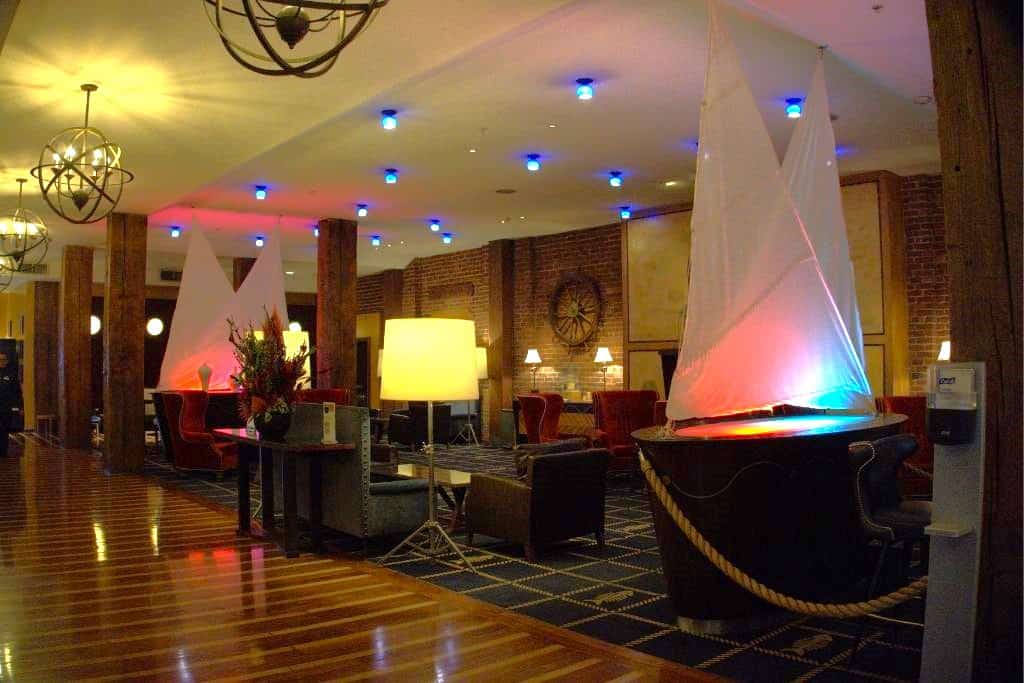 A hotel lobby featuring eclectic decor with modern lighting, a large model sailboat with illuminated sails, and a mix of traditional and contemporary furnishings.