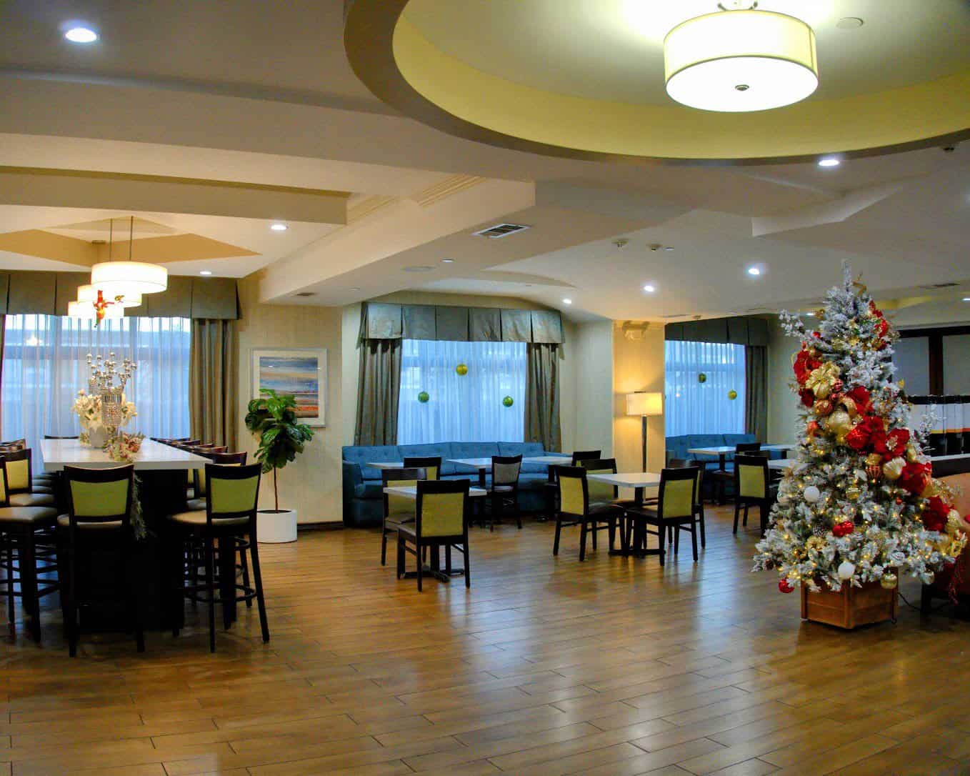 A cozy dining area at Hampton Inn LAX Hawthorne in Los Angeles, decorated with festive holiday touches, including a Christmas tree.