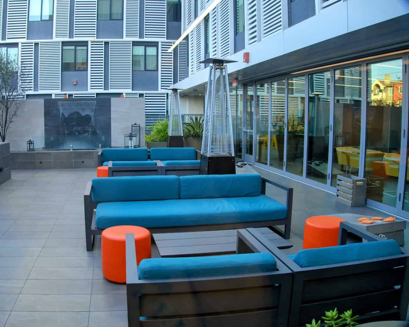 A modern outdoor seating area at Hotel Mariposa in Los Angeles, featuring vibrant blue couches, orange accent tables, and a sleek patio design.