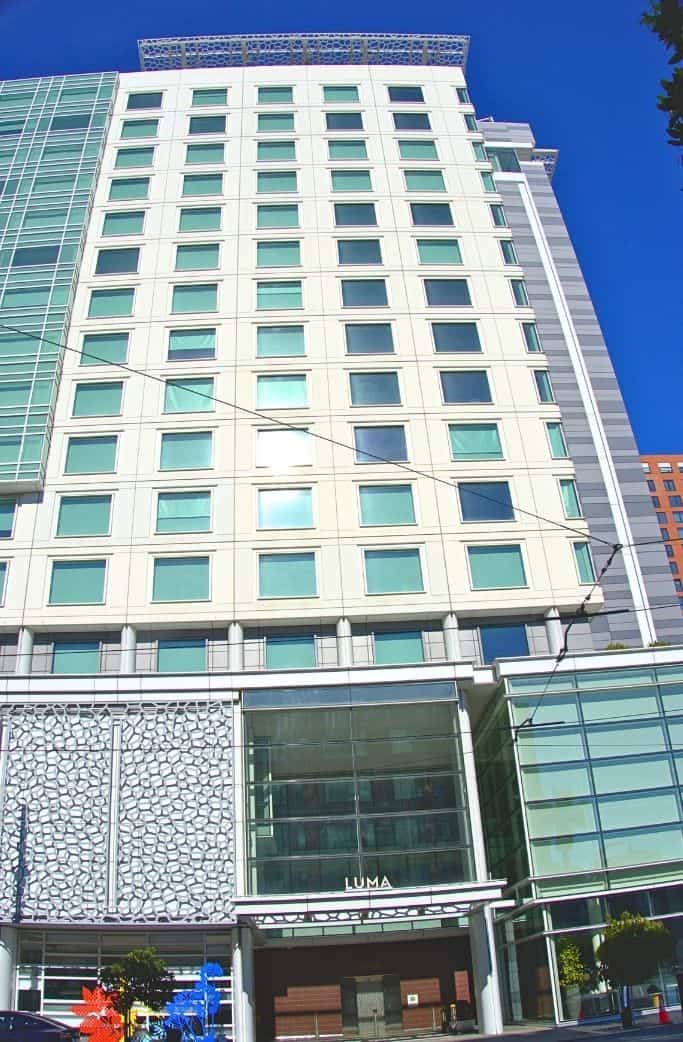 A modern high-rise building with a distinctive architectural design, featuring a patterned façade at the base and a series of uniform windows stretching upwards into the clear blue sky, representing contemporary urban development.