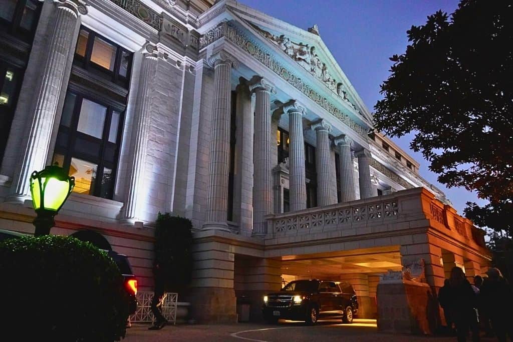 A historic hotel's grand entrance at dusk, with classical columns and ornate detailing illuminated by ambient lighting, creating a majestic and welcoming atmosphere.