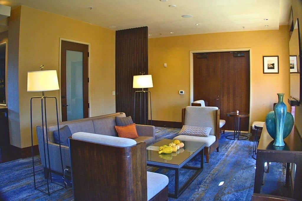 A lounge area with contemporary furniture, including sofas and chairs around a central coffee table, with a lamp stand on either side, and decorative vases adding to the ambiance.