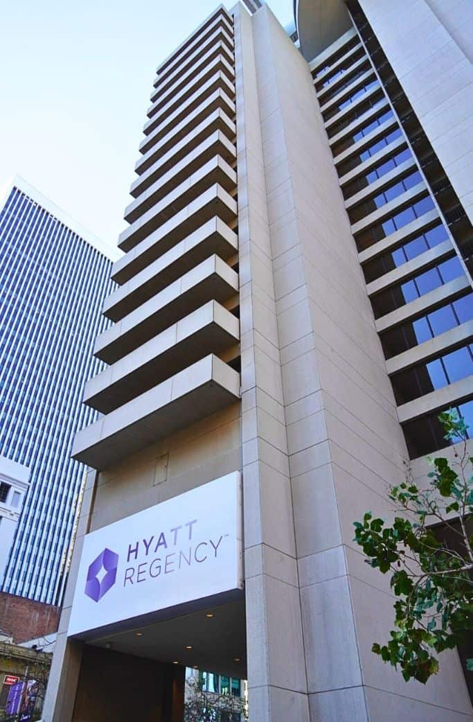 The facade of the Hyatt Regency hotel, a tall building with distinctive, layered architecture and the hotel's sign prominently displayed near the entrance.