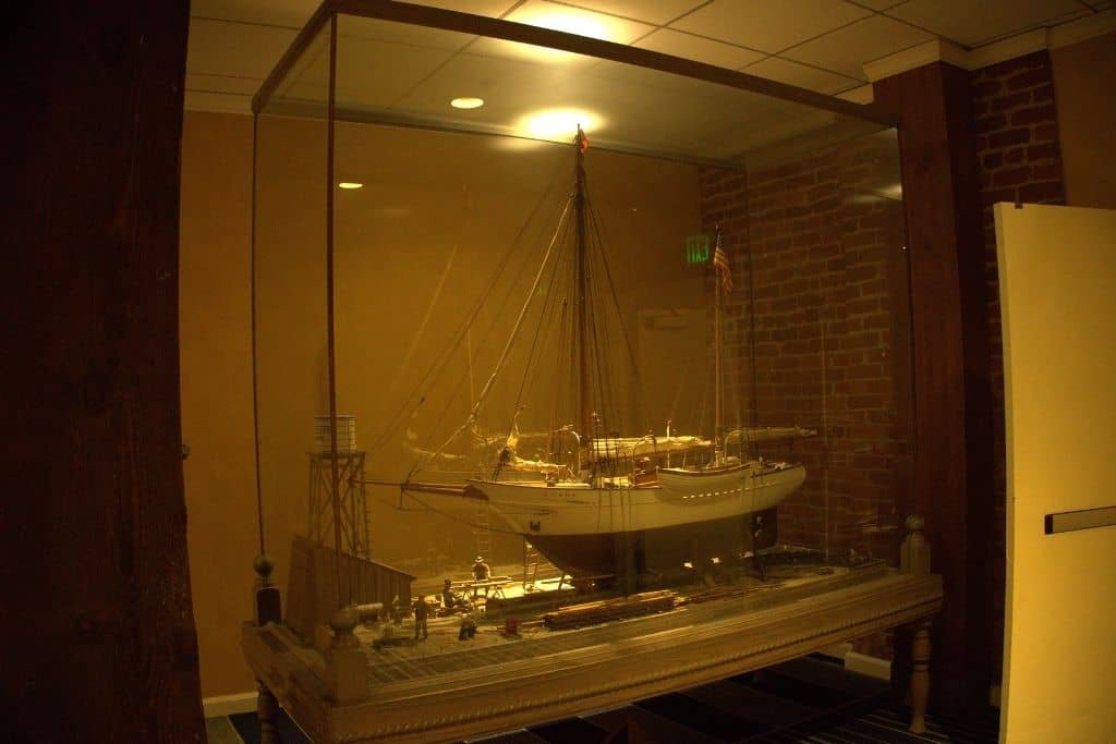 A large model sailboat is displayed within a glass case against a brick wall, softly lit by overhead lighting, providing a nautical touch to the space.