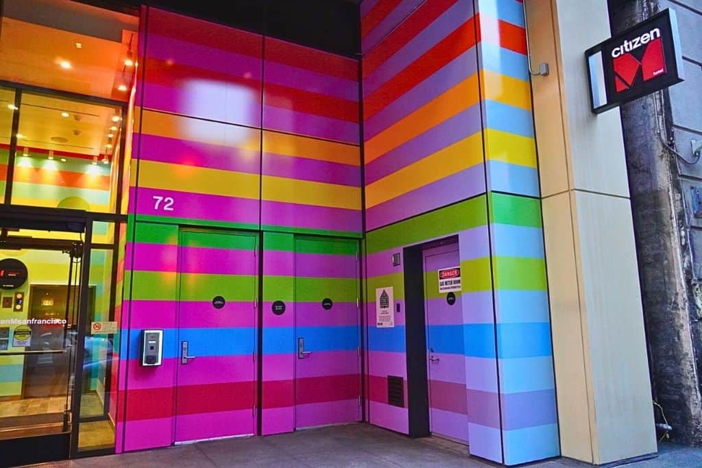 A strikingly colorful entrance with a door framed by vertical stripes in a rainbow of hues, labeled "72" and displaying signage for CitizenM San Francisco.
