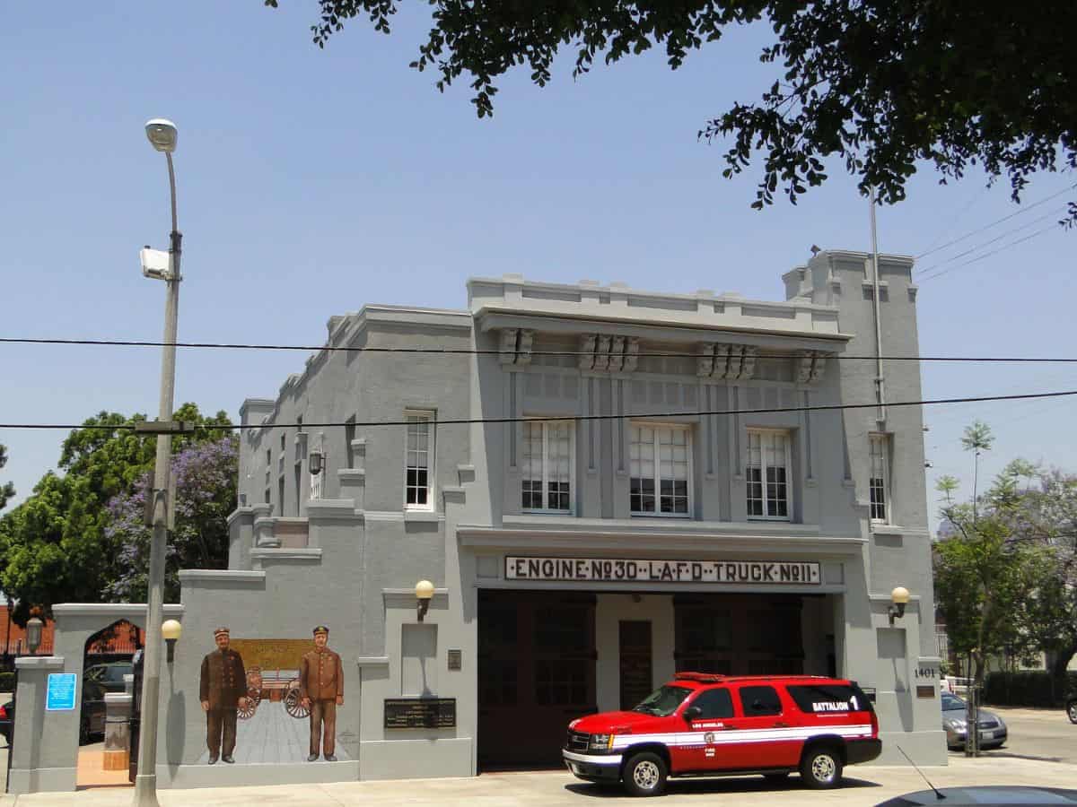 Historic fire station building with a gray facade, "Engine No. 30 L.A.F.D." written above, and a red fire department SUV parked outside.