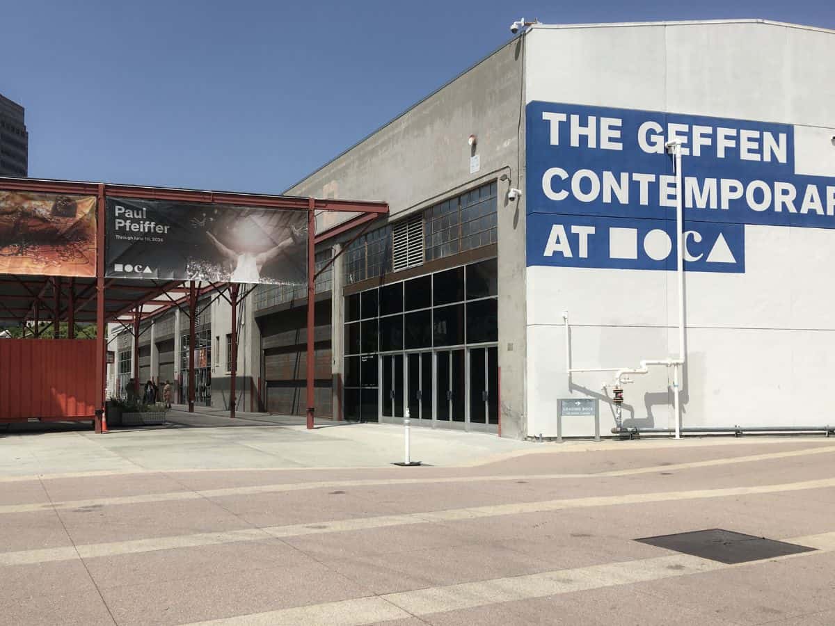 Exterior view of the Geffen Contemporary museum in Los Angeles, featuring its industrial-style architecture and a bold blue sign on the wall.