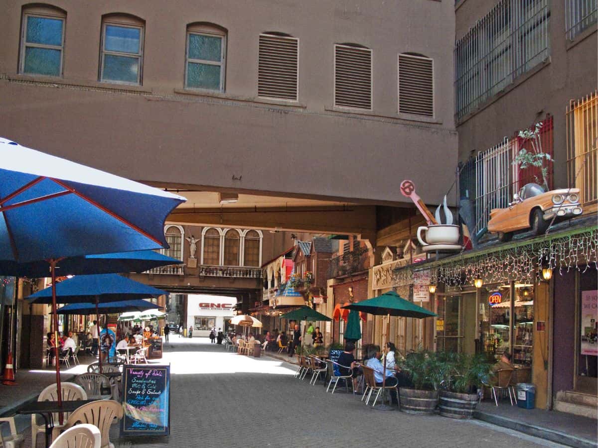  Outdoor dining area in St. Vincent Court, a hidden alley in downtown Los Angeles, featuring colorful umbrellas, decorative storefronts, and a vintage, European-style ambiance.
