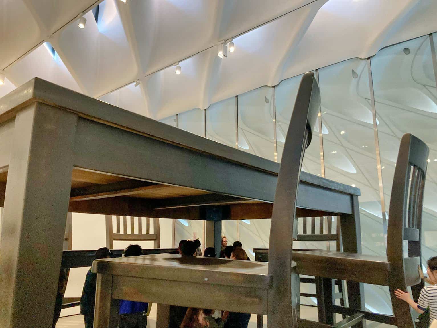 A view of a surreal art installation featuring a giant table and chairs, creating a whimsical and playful atmosphere inside The Broad museum.