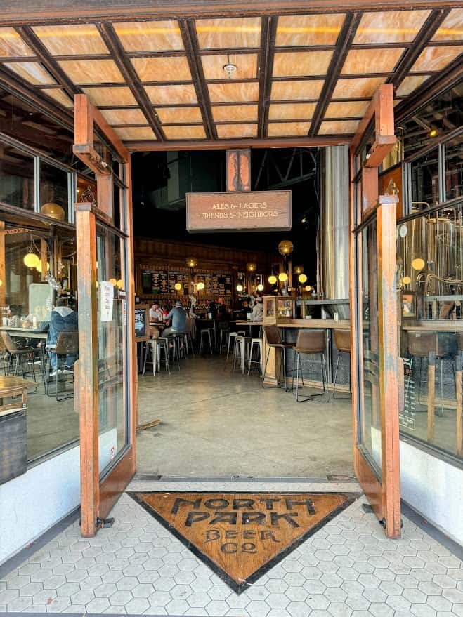 Entrance to North Park Beer Co. with a welcoming open door, a sign reading 'Ales & Lagers Friends & Neighbors,' embodying the community spirit of the best bars in North Park San Diego