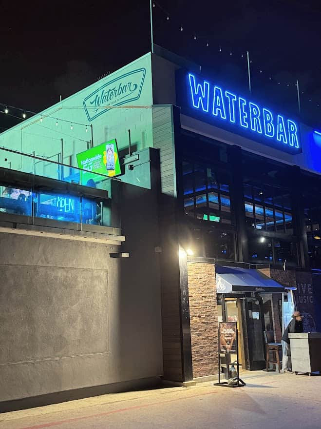The exterior of Waterbar, one of the best restaurants in Pacific Beach San Diego, showcasing its modern facade with a vibrant blue 'WATERBAR' neon sign illuminating the night