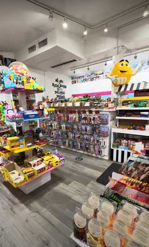The photo shows the inside of a vibrant candy store, one of the sweetest spots among the best things to do in Seaport Village San Diego. With shelves stocked full of colorful candies and treats, the shop invites visitors of all ages to indulge in a world of sugary delights. A cheerful yellow M&M character adds to the fun atmosphere, waving at customers from its perch above the candy displays. The bright interior and varied selection make it a must-visit for anyone with a sweet tooth exploring Seaport Village