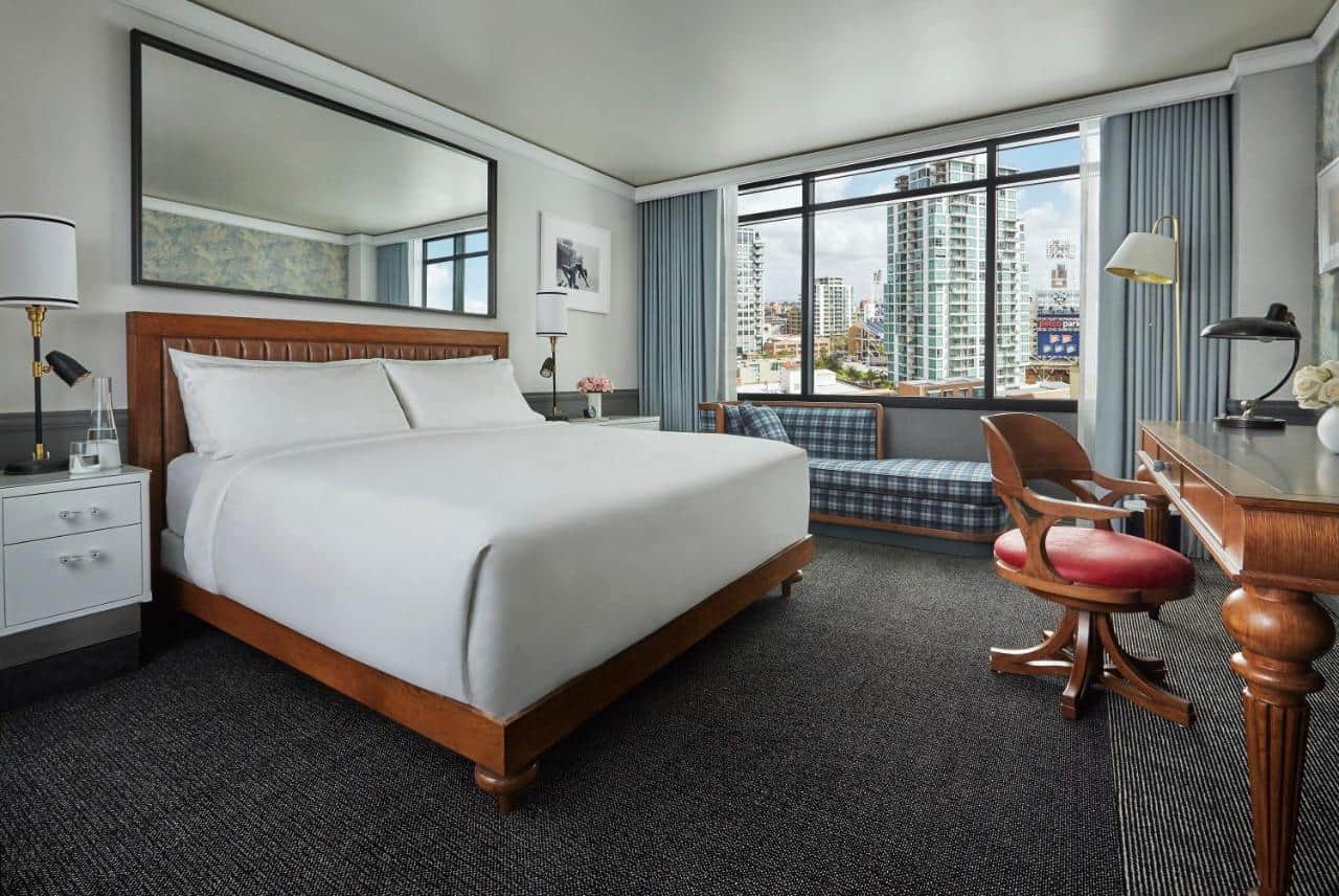 Elegantly appointed hotel room with a large king-sized bed, classic wood furnishings, window seating area offering city views, and tasteful art decor enhancing the sophisticated ambiance.