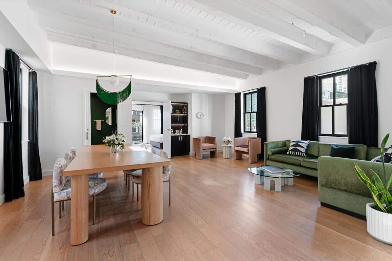 Spacious modern living room with exposed white beams, a plush green sofa, and wooden dining set, evoking a sleek yet cozy urban home atmosphere.