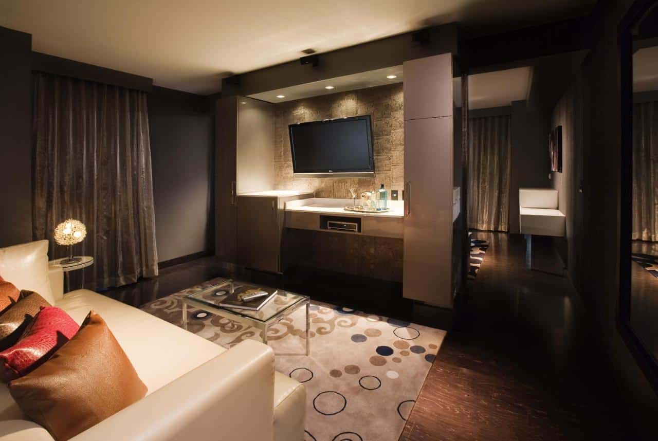 Dark-toned, intimate hotel suite with modern furnishings, mood lighting, and an open-concept bath area for a luxurious stay.