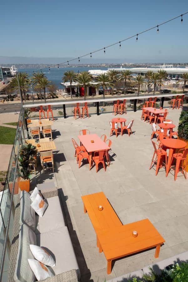 Rooftop terrace with bold orange furniture, offering a refreshing outdoor ambiance and a stunning view of the waterfront and palm trees.