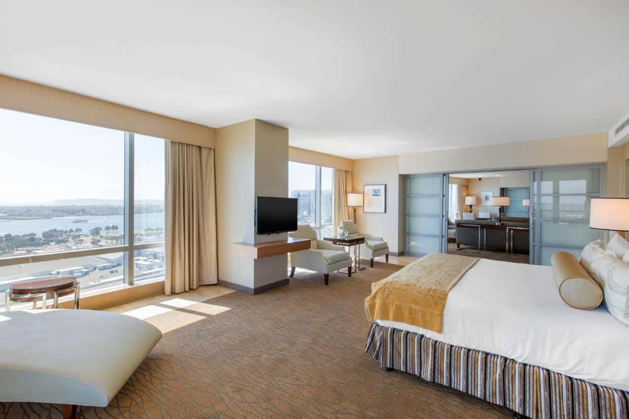 Bright and airy hotel room with panoramic windows offering expansive water views, a king-sized bed, and a comfortable seating area.