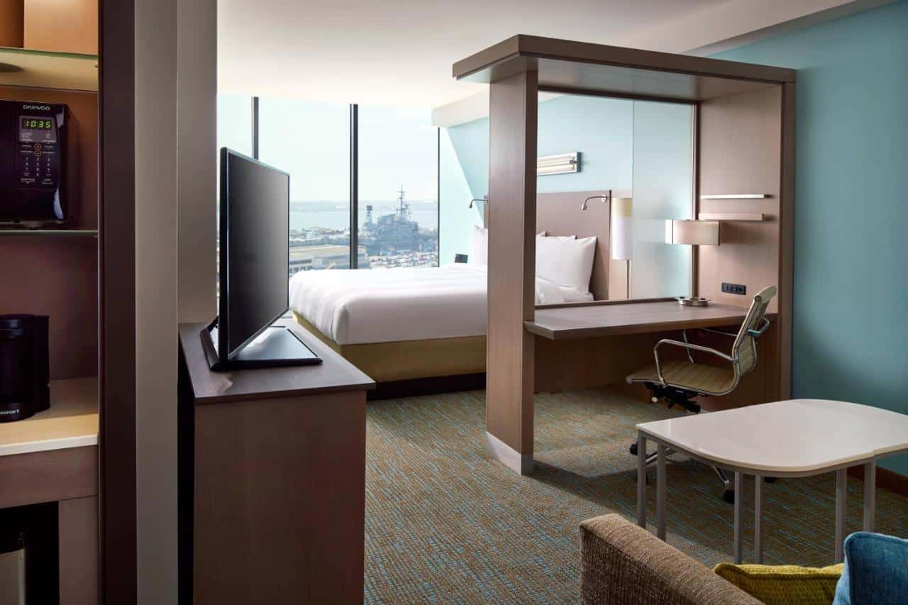 Compact and efficient hotel workspace with a floating bed design, boasting city and harbor views through large windows.