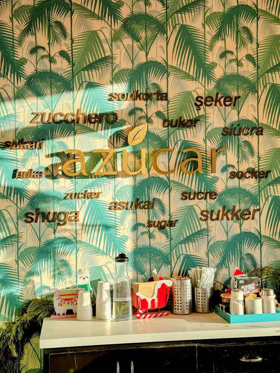 Inside Azucar in Ocean Beach San Diego with a wall that has tropical trees and the word 'sugar' in many languages, showing how the café brings sweet flavors from all over the world