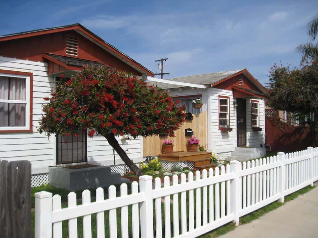 Quaint and colorful front facade of a beloved Airbnb in Ocean Beach San Diego, showcasing a classic white picket fence and vibrant flower beds enhancing its welcoming porch