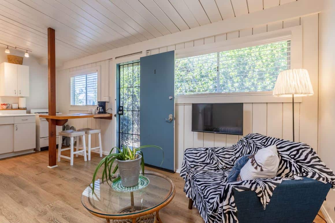 Charming and cozy interior of one of the best Airbnbs in Ocean Beach San Diego, showcasing a bright living area with a wood-paneled ceiling, white walls, a vintage kitchenette, and vibrant blue accents
