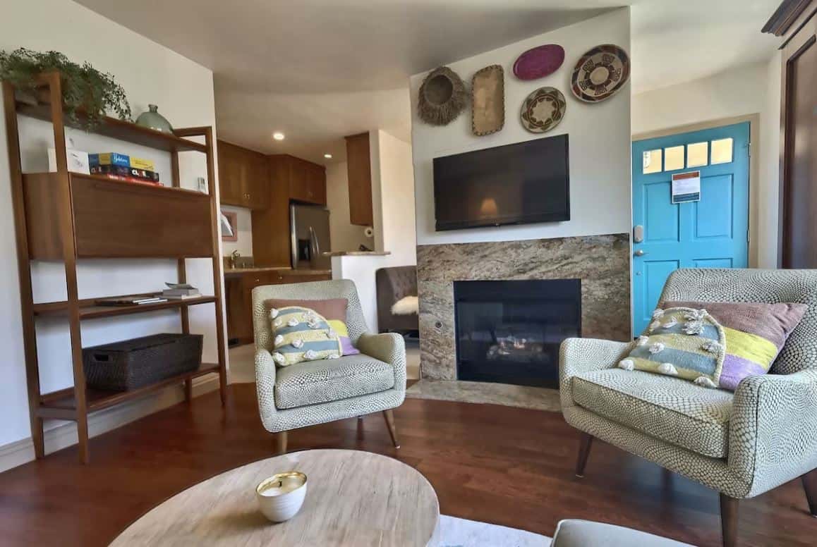Elegant living room in one of the best Airbnbs in Ocean Beach San Diego, showcasing a natural stone fireplace, stylish mid-century modern furniture, and unique wall decorations