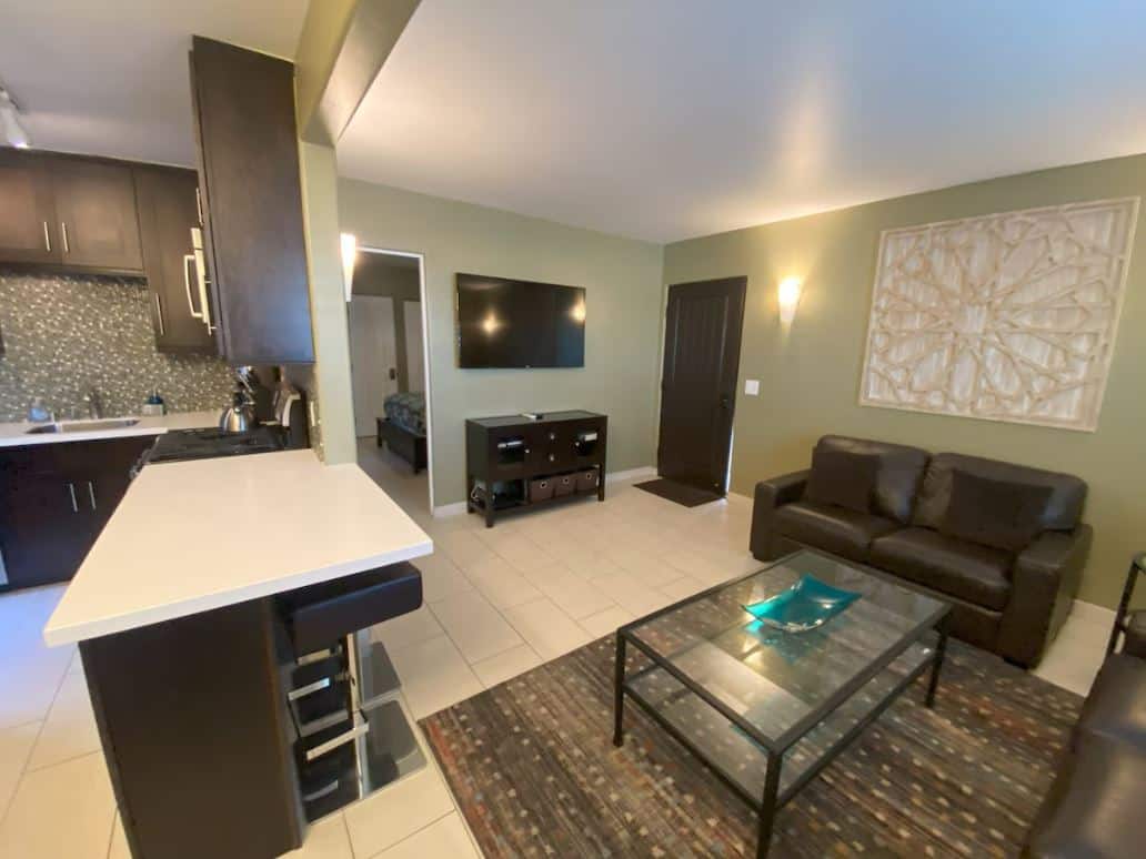 Modern living area inside one of the best Airbnbs in Ocean Beach San Diego, featuring a sleek kitchen with a breakfast bar and a cozy living room with dark leather furniture and a large wall-mounted TV