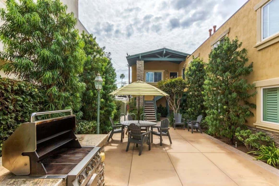 Spacious outdoor patio with a large dining table under a stylish umbrella, part of one of the best Airbnbs in Ocean Beach San Diego, surrounded by lush plants