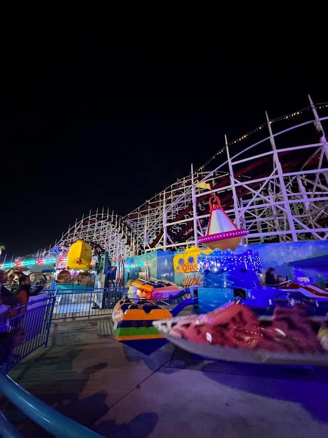 A view of the kiddie rides area at Belmont Park, with colorful, spinning rides and the Giant Dipper roller coaster in the background, showcasing family-friendly things to do in Belmont Park, Mission Beach.