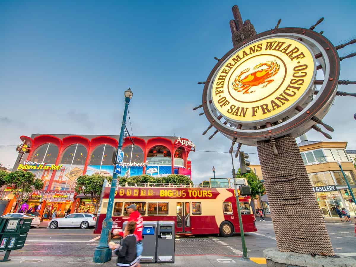 The iconic Fisherman's Wharf sign with bustling activity and colorful buildings in the background. Visiting Fisherman's Wharf is a top thing to do in San Francisco for its dining, shopping, and entertainment.