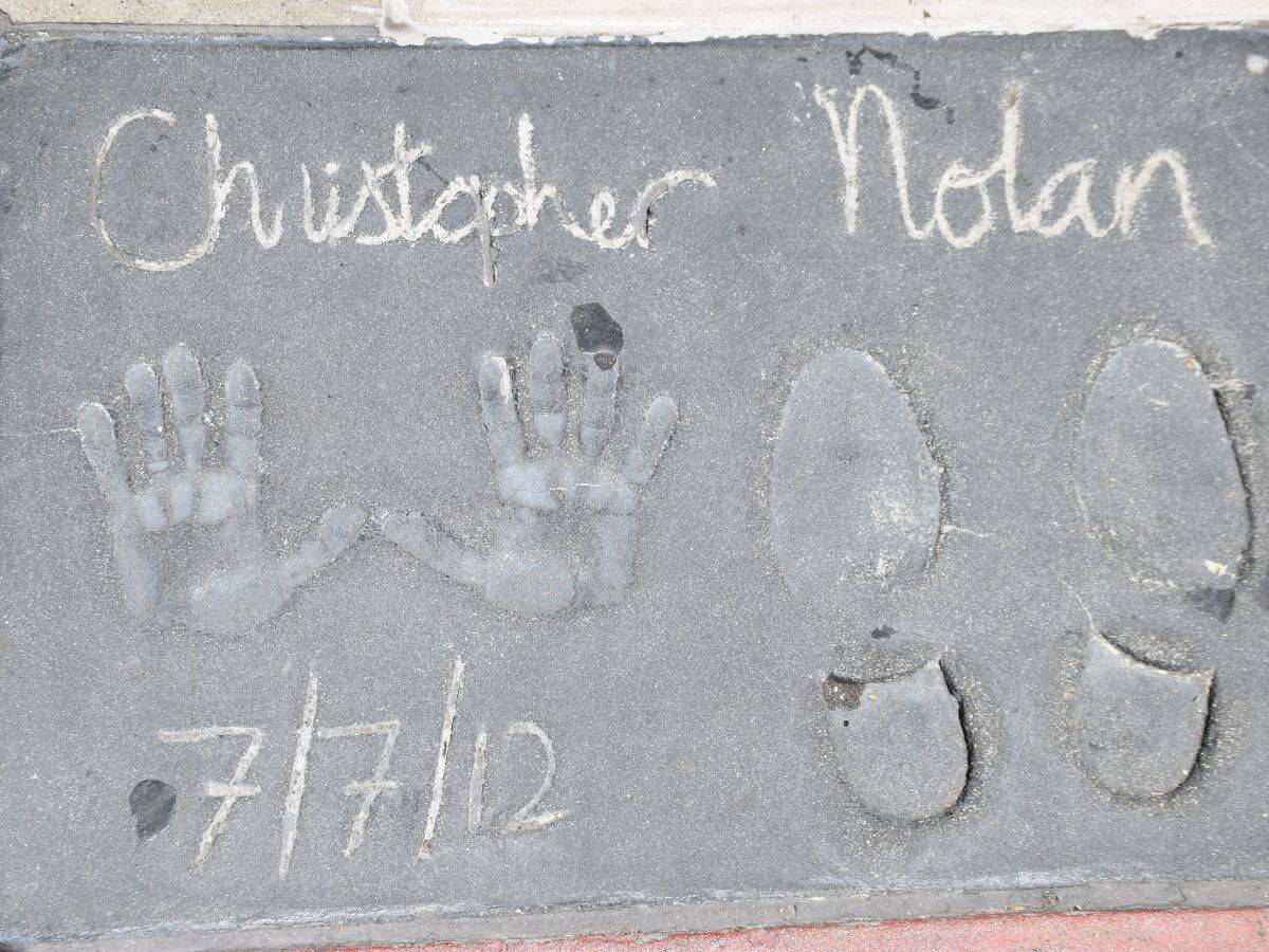 A close-up of Christopher Nolan's handprints and footprints cemented in front of TCL Chinese Theatre in Los Angeles, with his name and the date "7/7/12" etched in the cement, part of the famous Hollywood landmark.