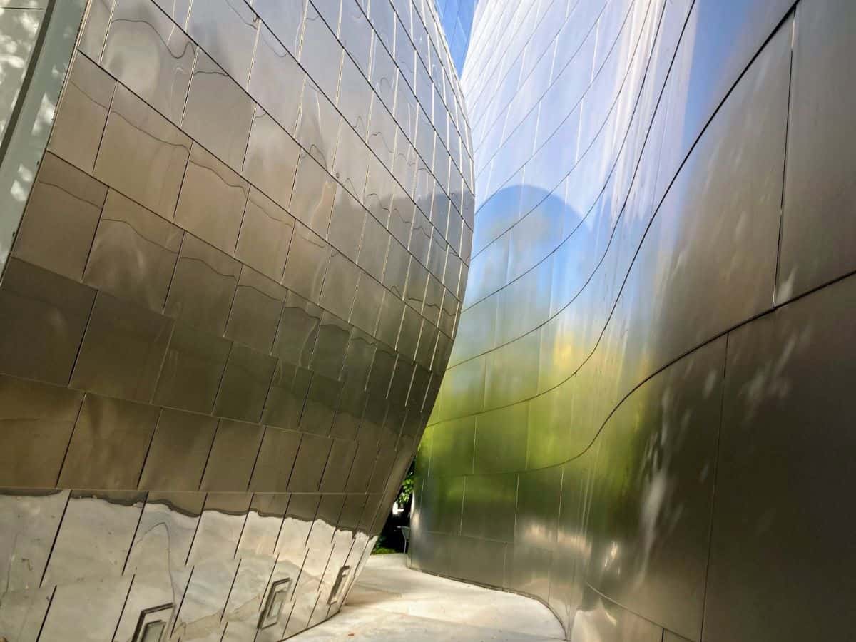 Close-up view of the Walt Disney Concert Hall's metallic exterior in Los Angeles, showcasing the building's dynamic and flowing architecture with reflective surfaces that capture and bend the light, creating a surreal walking path.