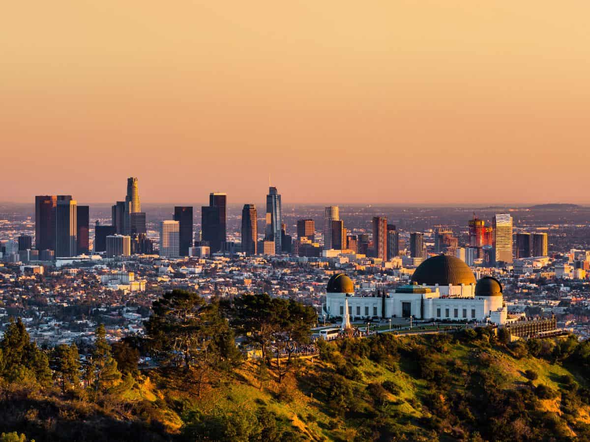 Sunset view of Los Angeles skyline with the iconic Griffith Observatory in the foreground. The city's dense buildings are bathed in golden light, showcasing a popular thing to do in Los Angeles: visiting this historic site for panoramic views.