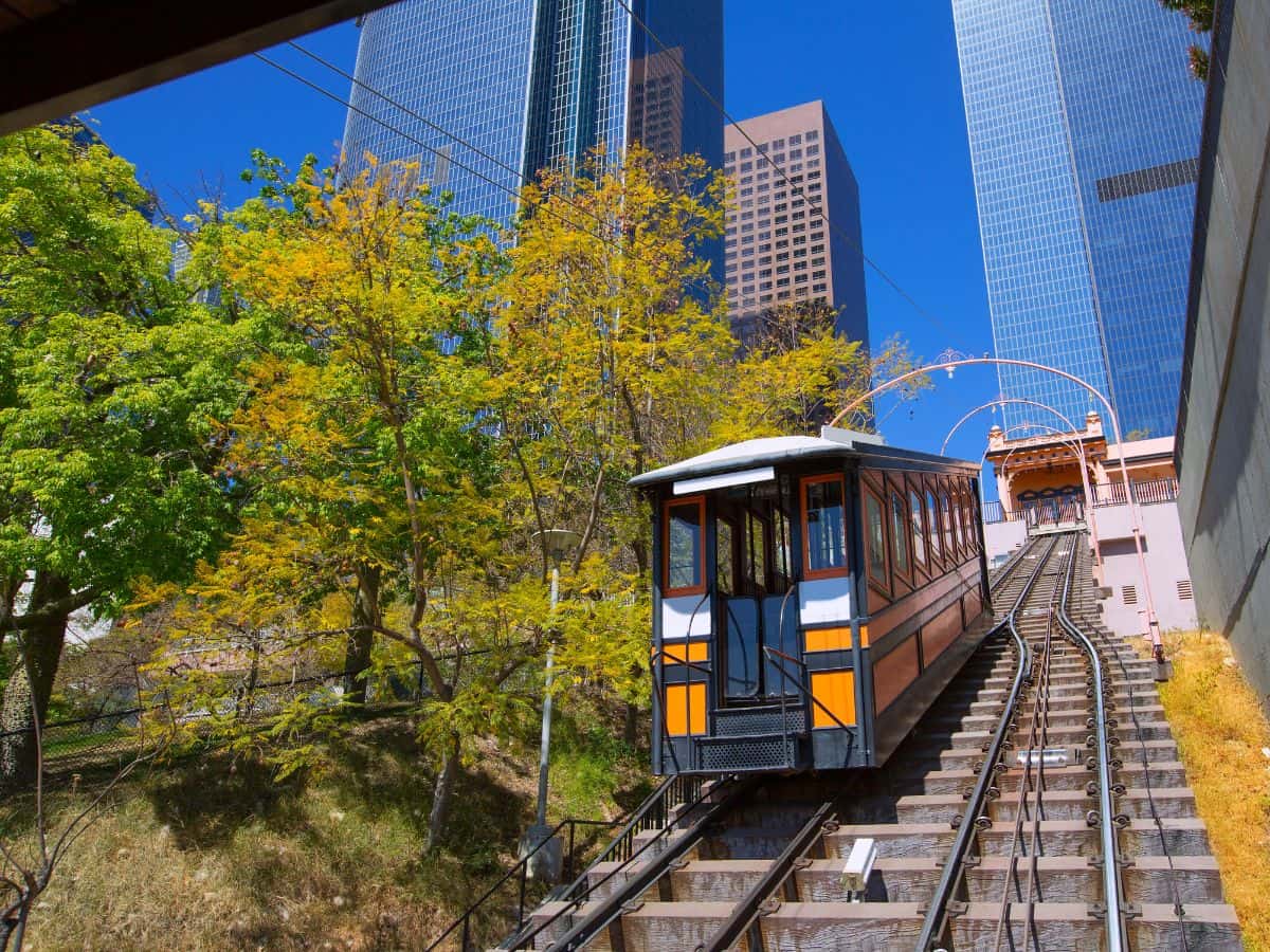 Angels Flight, a historic funicular railway in Los Angeles, seen ascending between lush green trees and high-rise buildings, offering a short but historic ride and a unique thing to do in Los Angeles.