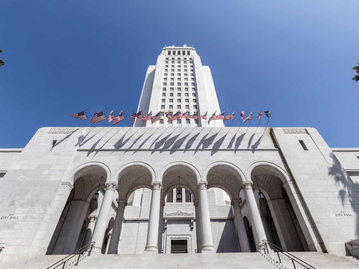 Los Angeles City Hall, a prominent architectural landmark, standing tall with numerous American flags fluttering in front.