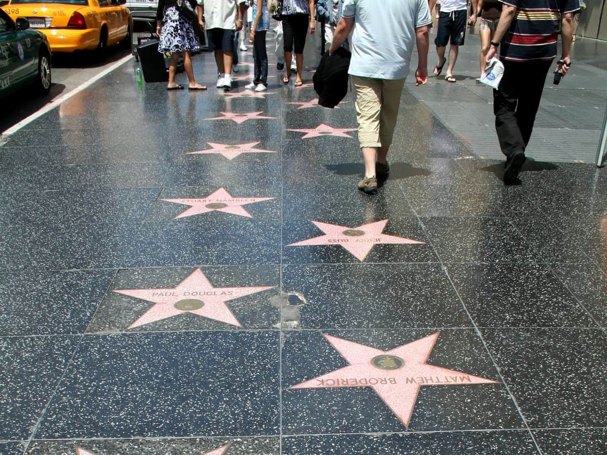 People walking on the Hollywood Walk of Fame, viewing stars named after famous celebrities embedded in the sidewalk, a quintessential thing to do in Los Angeles.