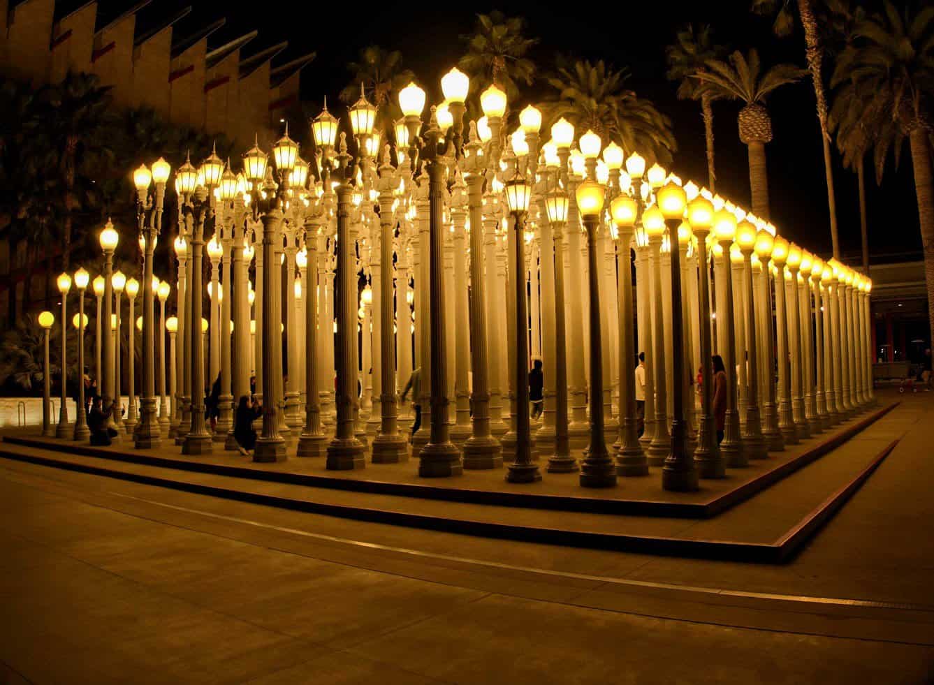 Nighttime view of the Urban Light installation at the Los Angeles County Museum of Art (LACMA), featuring rows of restored street lamps that light up beautifully against the dark sky.