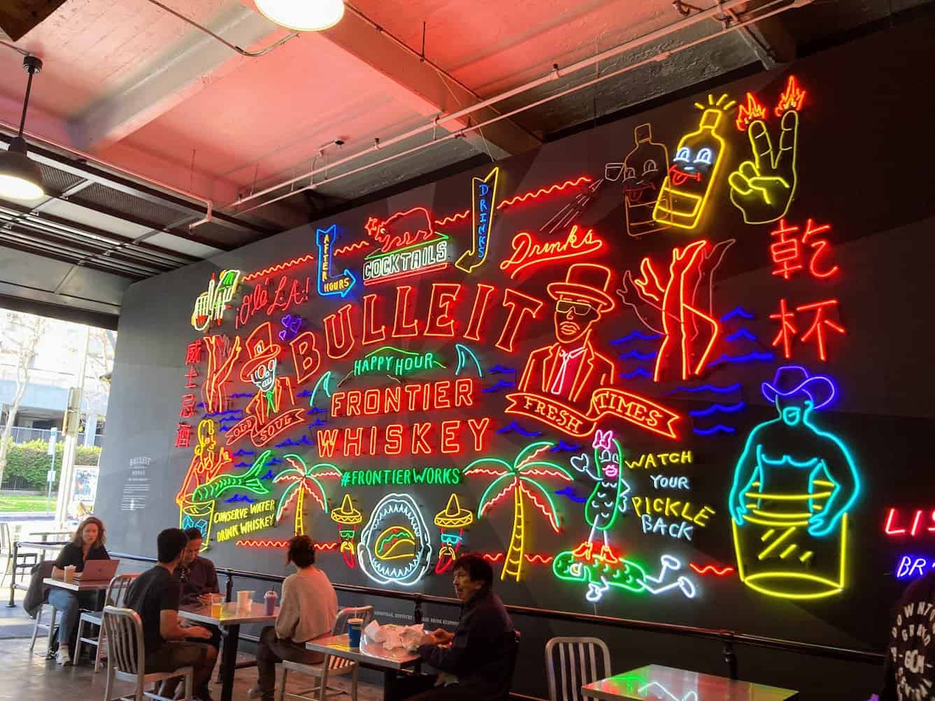 Vibrant neon art installation at Grand Central Market in Los Angeles, featuring colorful and whimsical signs for whiskey and cocktails. The artwork creates a lively and inviting atmosphere, making it a visually appealing thing to do in Los Angeles for both locals and visitors seeking a unique dining and entertainment experience.