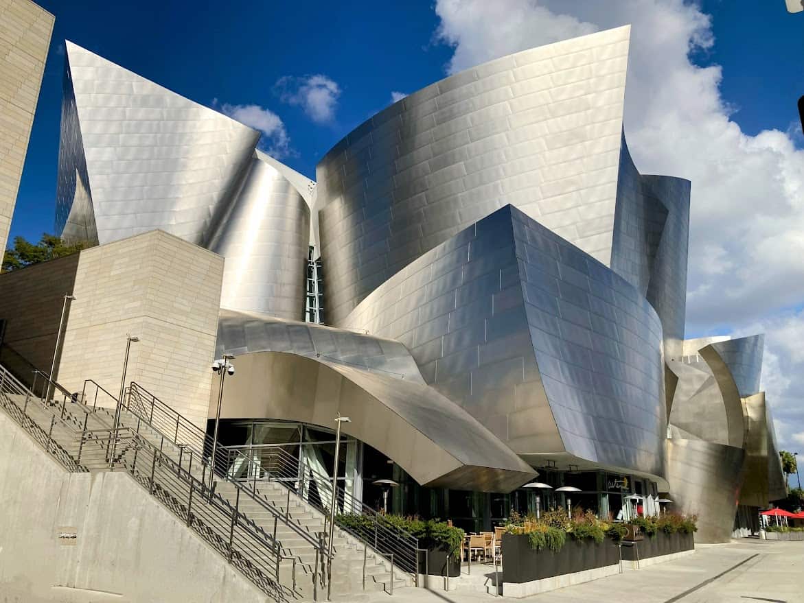 The Walt Disney Concert Hall in Los Angeles, known for its striking architecture with sweeping metallic surfaces that capture the California sunlight, creating a visually dynamic environment.