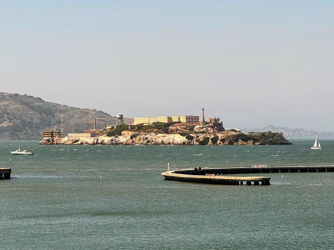 A distant view of Alcatraz Island as seen from the mainland, showcasing the historic prison against a backdrop of the San Francisco Bay. Touring Alcatraz Island is a fascinating historical experience and a top thing to do in San Francisco.