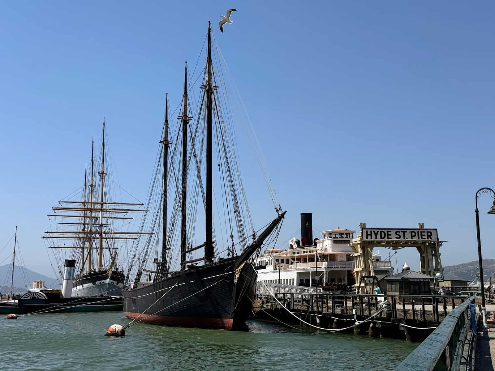 Historic ships moored at Hyde Street Pier in San Francisco, part of the maritime museum with the cityscape in the background. Visiting this pier is a fascinating thing to do in San Francisco, offering a glimpse into the city’s nautical history.