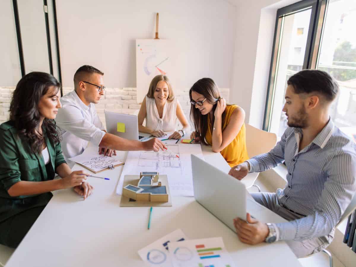 A group of professionals in a bright, modern office, collaborating over architectural plans. High labor costs, due to California's wage standards, impact the cost of services and products, contributing to why California is so expensive.