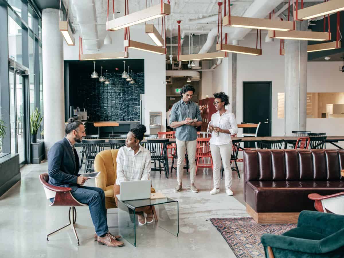 A group of professionals meeting in a stylish, modern office space with large windows and contemporary furniture. Higher-paying jobs in California's competitive job market drive up living costs, explaining why California is so expensive.