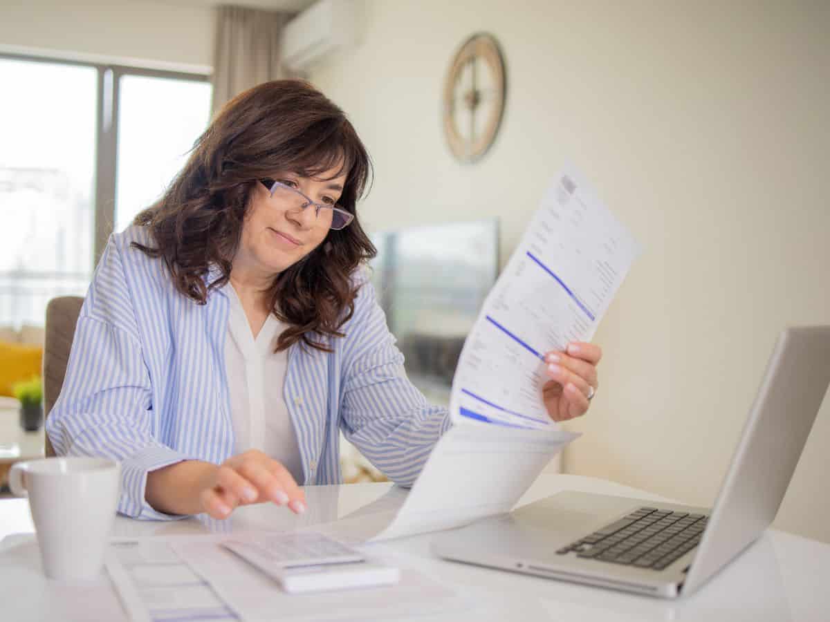 A woman reviewing bills at her kitchen table, looking slightly concerned. California's high sales tax rate impacts daily living costs, which is part of why California is so expensive.