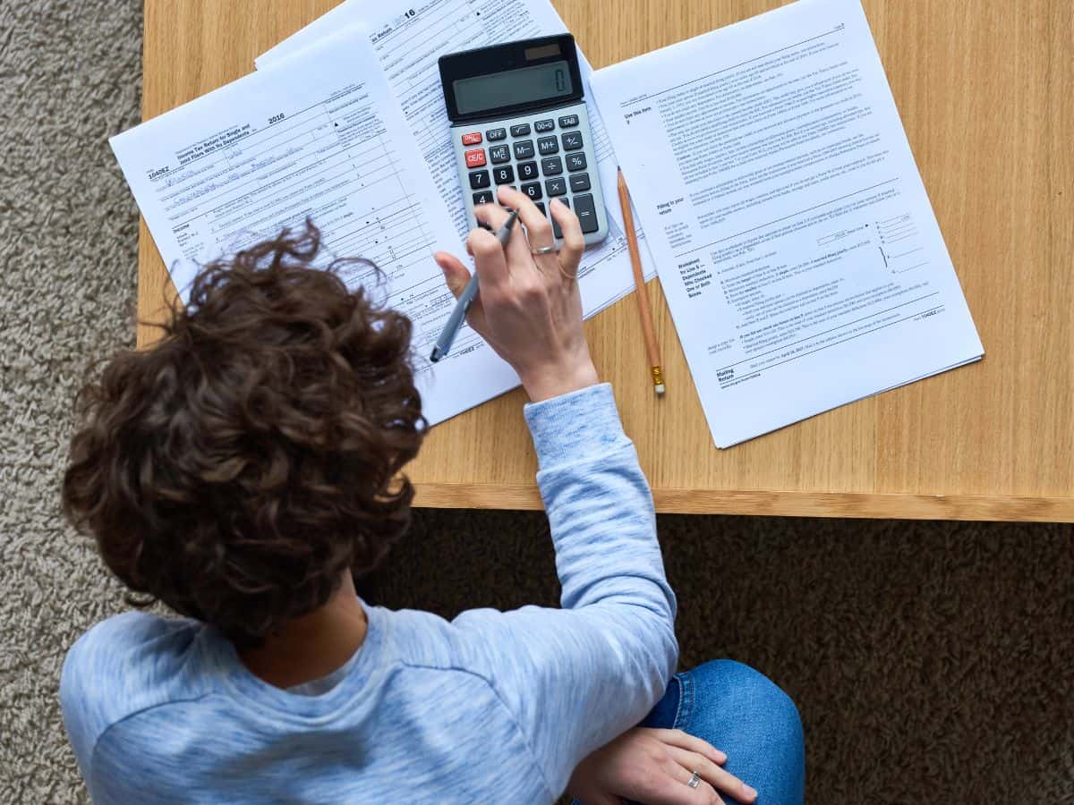 A person sitting at a table, using a calculator to work through financial documents. High income tax rates in California illustrate another reason why the state is so expensive.