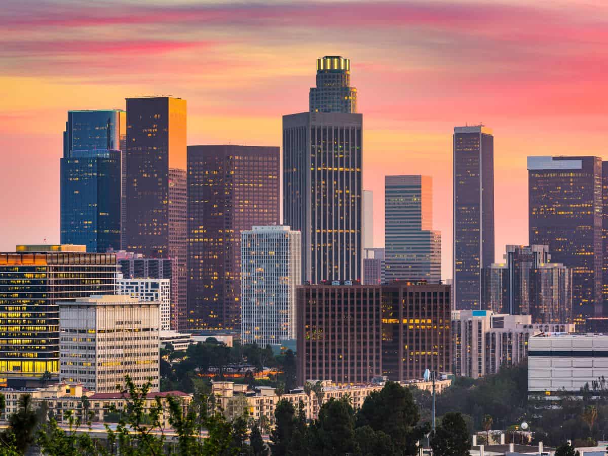 The downtown skyline at sunset, with tall buildings illuminated by the fading light. As the largest economy in the country, California's thriving business environment increases living costs, explaining why California is so expensive.