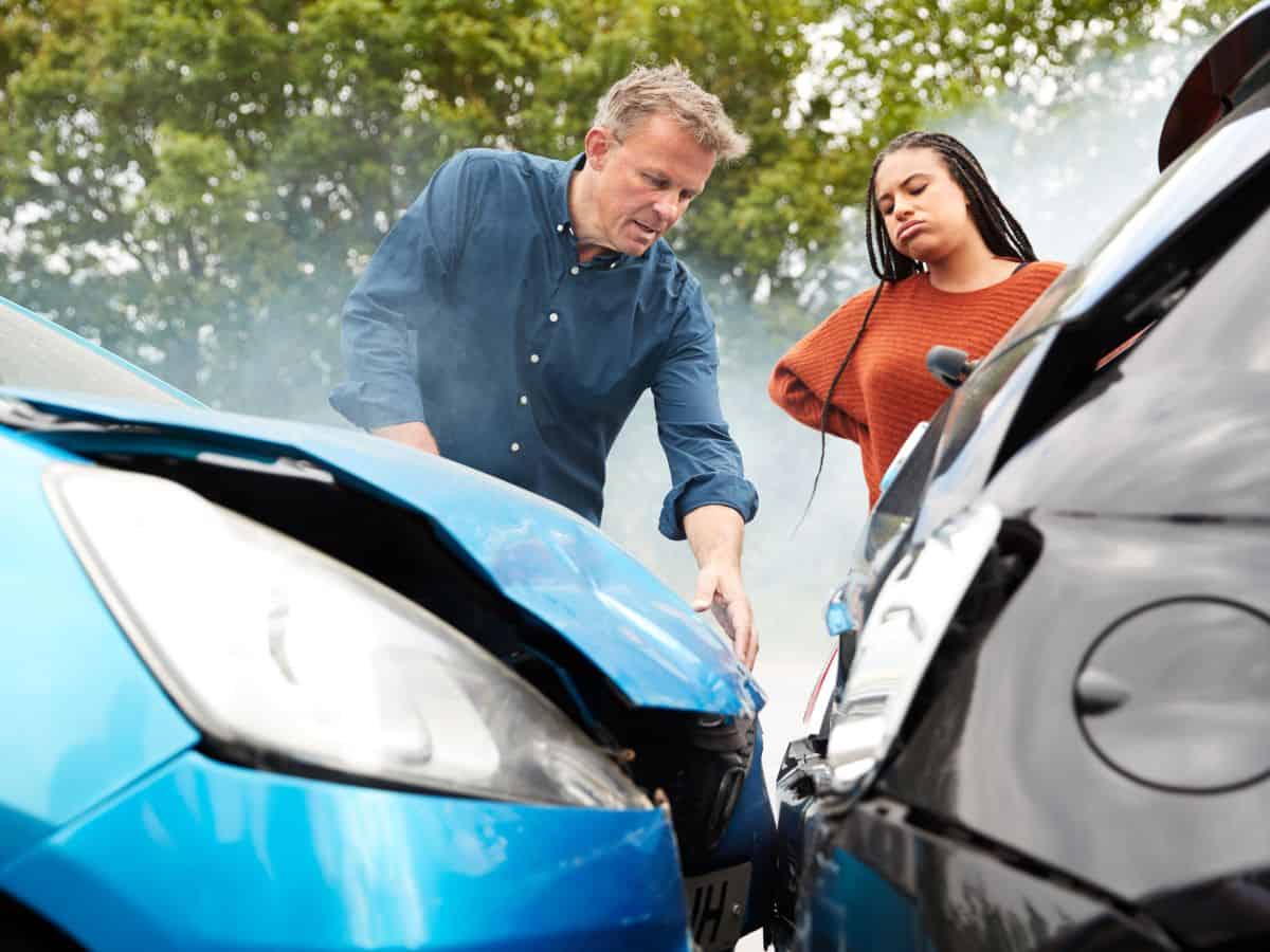 A man and a woman inspecting damage after a car accident. High car accident rates in California drive up insurance premiums, adding to the reasons why California is so expensive.
