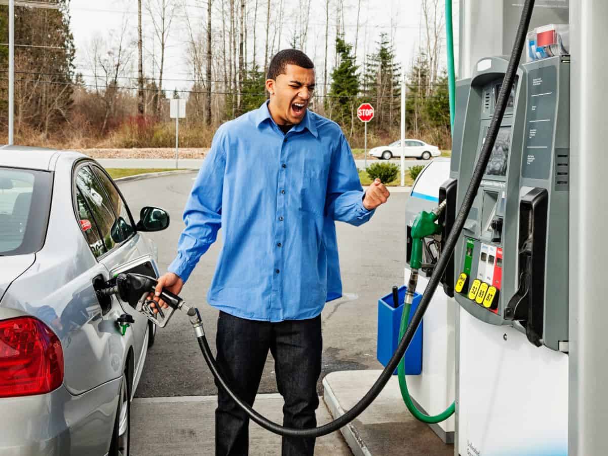 A man stands at a gas station, visibly frustrated and angry as he pumps gas into his car. His clenched fists and intense expression reflect the irritation many California residents experience due to high fuel prices, which are a key factor in the broader issue of California's high cost of living. This scene highlights one of the reasons behind the question, "Why Is California So Expensive? Here Are 25 Eye-Opening Reasons."