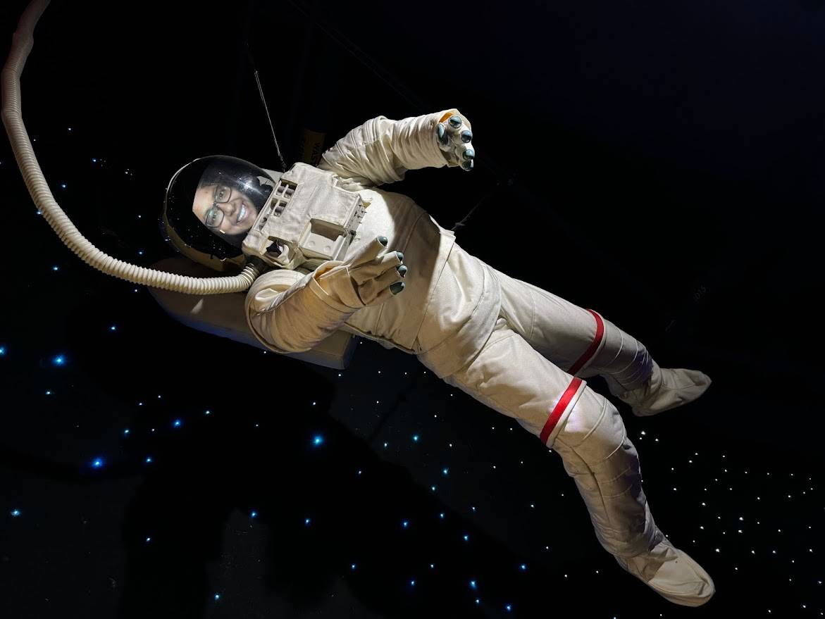 Shreeyeh posing in an astronaut suit exhibit at The Tech Interactive, floating as if in zero gravity, showcasing one of the exciting reasons to visit The Tech Interactive.